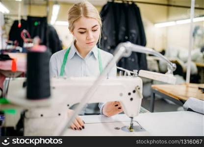 Dressmaker sews fabrics on a sewing machine. Tailoring or dressmaking on clothing factory, needlework, female seamstress in workshop