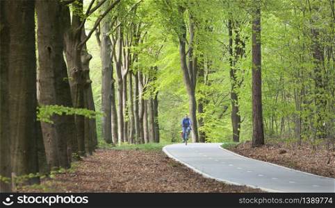 Driebergen, Netherlands, 26 april 2020: woman in blue on bike in spring forest on bicycle track
