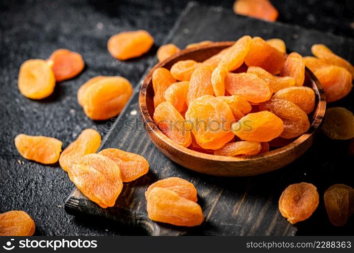 Dried apricots in a plate on a cutting board. On a black background. High quality photo. Dried apricots in a plate on a cutting board.