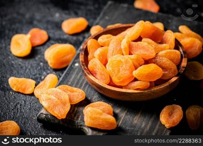 Dried apricots in a plate on a cutting board. On a black background. High quality photo. Dried apricots in a plate on a cutting board.