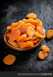 Dried apricots in a wooden plate on the table. On a black background. High quality photo. Dried apricots in a wooden plate on the table.