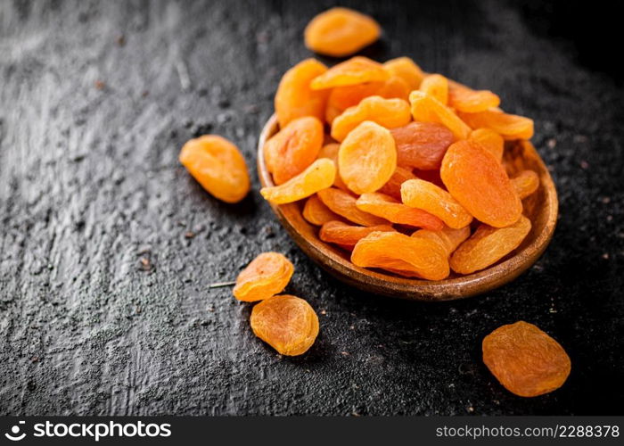 Dried apricots in a wooden plate on the table. On a black background. High quality photo. Dried apricots in a wooden plate on the table.