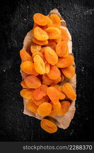 Dried apricots on a piece of paper on a table. On a black background. High quality photo. Dried apricots on a piece of paper on a table.