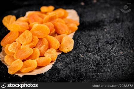 Dried apricots on a piece of paper on a table. On a black background. High quality photo. Dried apricots on a piece of paper on a table.