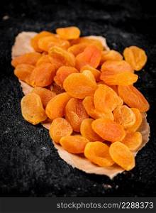 Dried apricots on a piece of paper on a table. On a black background. High quality photo. Dried apricots on a piece of paper on a table.