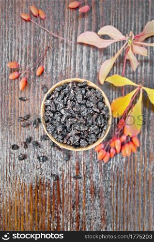 Dried black barberry in a bowl, sprigs with fresh berries and leaves on wooden board background from above