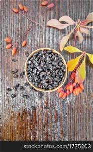Dried black barberry in a bowl, sprigs with fresh berries and leaves on wooden board background from above