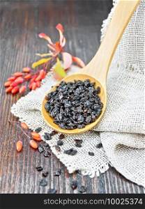 Dried black barberry in a spoon on sacking, sprigs with fresh berries and leaves on a brown wooden board background