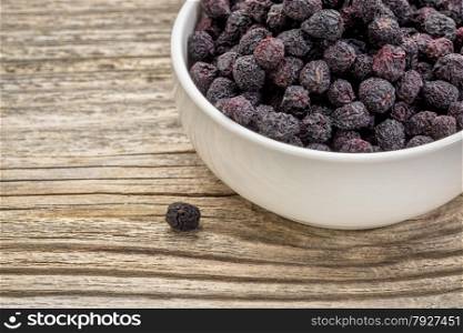 Dried chokeberry (aronia berry) in a small, ceramic bowl against grained wood