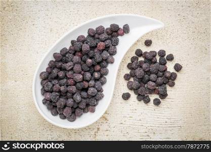 Dried chokeberry (aronia berry) in a teardrop shaped bowl against rustic barn wood