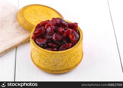 Dried cranberries in a wooden cup with a lid and burlap on a white wooden table