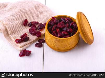 Dried cranberries in a wooden cup with a lid and burlap on a white wooden table