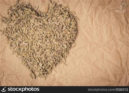 Dried fennel dill seeds heart shaped on paper surface with copy space. Fennel dill seeds heart shaped on paper surface