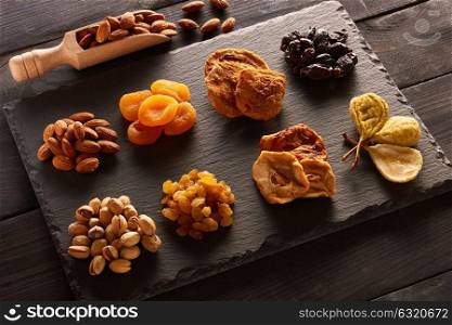 Dried fruits and nuts on slate plate over vintage rustic wooden background