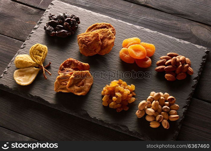 Dried fruits and nuts on slate plate over vintage rustic wooden background