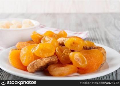 Dried fruits in white plate on a wooden background. Candied pineapple, lemon, apricot, figs.