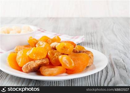 Dried fruits in white plate on a wooden background. Lemons, apricots and figs.