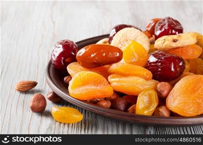 Dried fruits on a wooden background. Dates, lemon, apricots, figs and nuts in a clay plate.