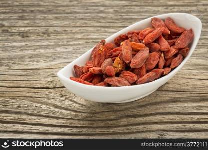 dried goji berries in a small ceramic bowl against grained wood