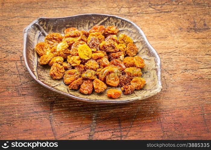 dried goldenberries in a ceramic leaf shaped bowl against rustic scratched wood