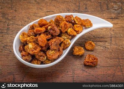 dried goldenberries in a ceramic teardrop shaped bowl against rustic scratched wood