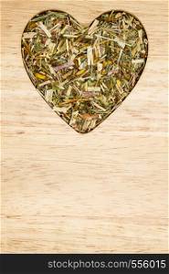 Dried herb leaves heart shaped on wooden surface. Herbaceous dry aromatic plant. Healthy cooking concept.. Dried herb leaves heart shaped on wooden surface