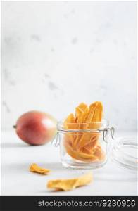 Dried mango pieces in glass jar and raw fruit on light background.Macro