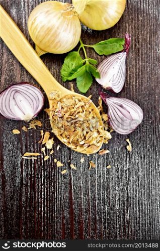 Dried onion flakes in a spoon, purple and yellow onions, basil on wooden board background from above