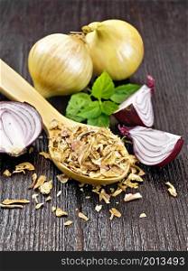 Dried onion flakes in a spoon, purple and yellow onions, basil on dark wooden board background