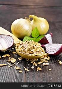 Dried onion flakes in a spoon, purple and yellow onions, basil on wooden board background