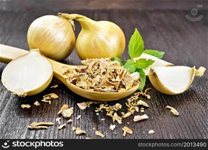 Dried onion flakes in a spoon, yellow onions, basil on wooden board background