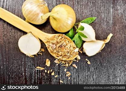 Dried onion flakes in a spoon, yellow onions, basil on wooden board background from above