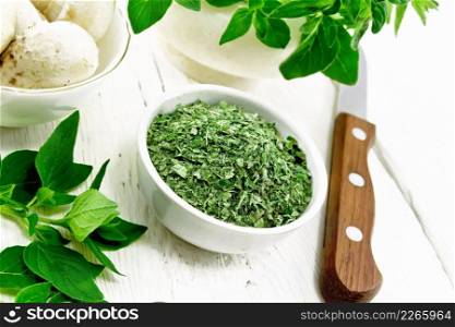 Dried oregano in bowl, oregano branches with leaves in a mortar, ch&ignons and a knife on wooden board background