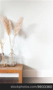 Dried p&as grass in glass vase on wooden table near white background, modern bright decoration for home interior, copy space,space for text. Dried p&as grass in glass vase on wooden table near white background, modern bright decoration for home interior, copy space
