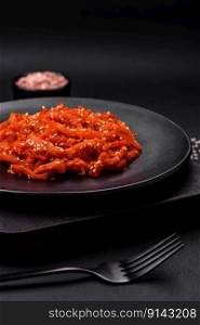 Dried squid chopped into slices and seasoned with sesame seeds and spices on a dark concrete background. Korean cuisine dish