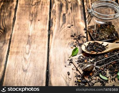 Dried tea jar with a tea spoon and green leaves. On wooden background.. Dried tea jar