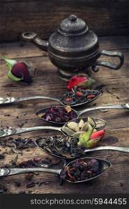 Dried tea leaves. Stylish spoons with variety of tea on vintage wooden board.