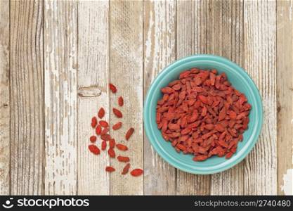 dried Tibetan goji berries (wolfberries) in a blue ceramic bowl on a grunge white painted wood surface