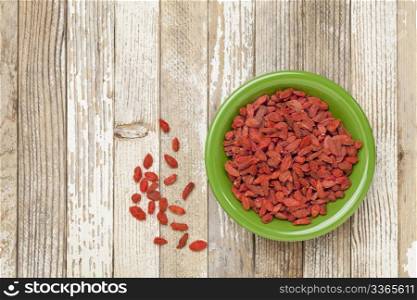 dried Tibetan goji berries (wolfberries) in a green ceramic bowl on a grunge white painted wood surface
