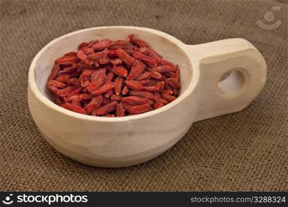 dried Tibetan goji berries (wolfberries) on a rustic unfinished wooden scoop, burlap background