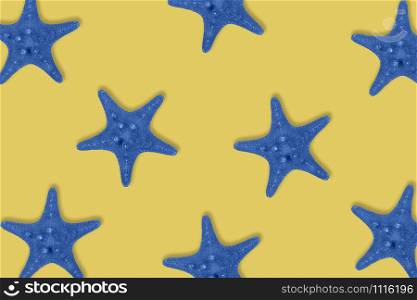 Dried toned in blue sea star fish pattern on yellow background. Top view, flat lay.. Dried toned in blue sea star fish pattern on yellow background.