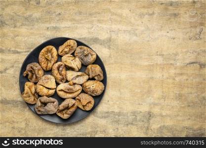 dried Turkish figs on a black plate against textured bark paper with a copy space