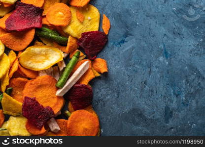 Dried vegetables chips from carrot, beet, parsnip and other vegetables on blue backgrounds. Organic diet and vegan food.
