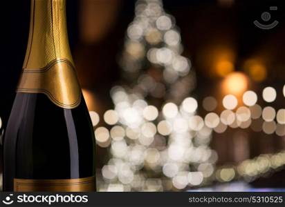 drink, alcohol and holidays concept - close up of bottle of champagne with blank golden label over christmas tree lights background. close up of champagne bottle over christmas lights
