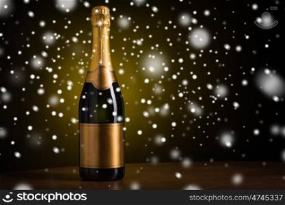 drink, alcohol, christmas, new year and winter holidays concept - bottle of champagne with blank golden label on wooden table over dark background and snow