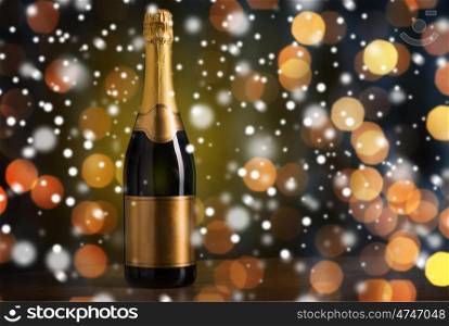 drink, alcohol, christmas, new year and winter holidays concept - bottle of champagne with blank golden label on wooden table over dark background with snow and lights