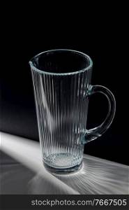drink and glassware concept - empty faceted glass jug on table over black background. empty faceted glass jug on table
