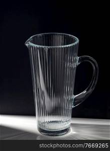 drink and glassware concept - empty faceted glass jug on table over black background. empty faceted glass jug on table