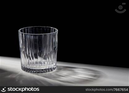 drink and glassware concept - empty faceted glass on table over black background. empty faceted glass on table