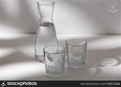 drink and glassware concept - two glasses and jug with water on white background with shadows. two glasses and jug with water on white background